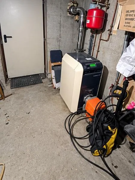 Chaufferie avant travaux : ancienne chaudière au sol, vase d’expansion rouge et matériel entreposé