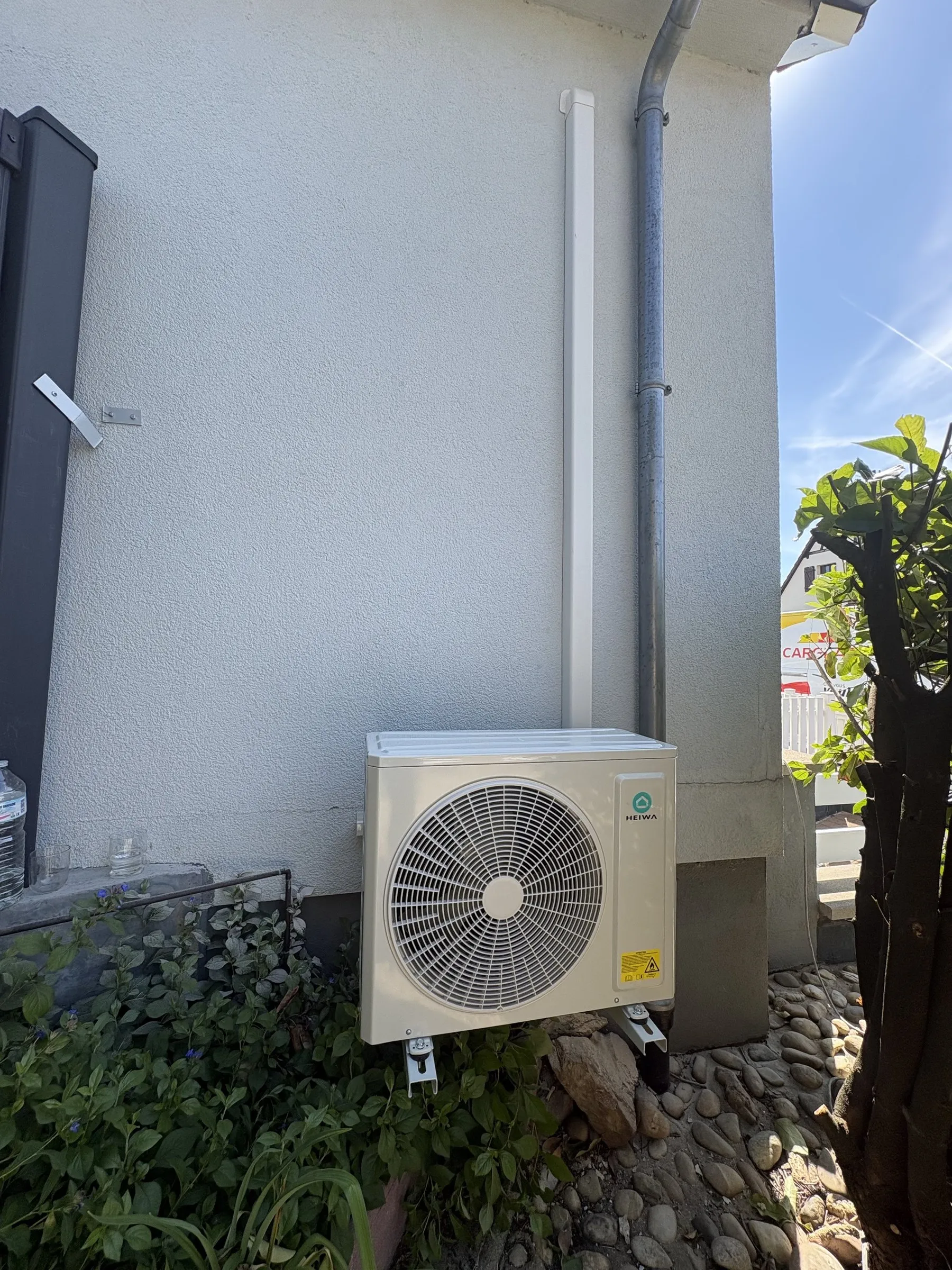 Unité extérieure de climatisation sur console murale au-dessus d’un massif de galets