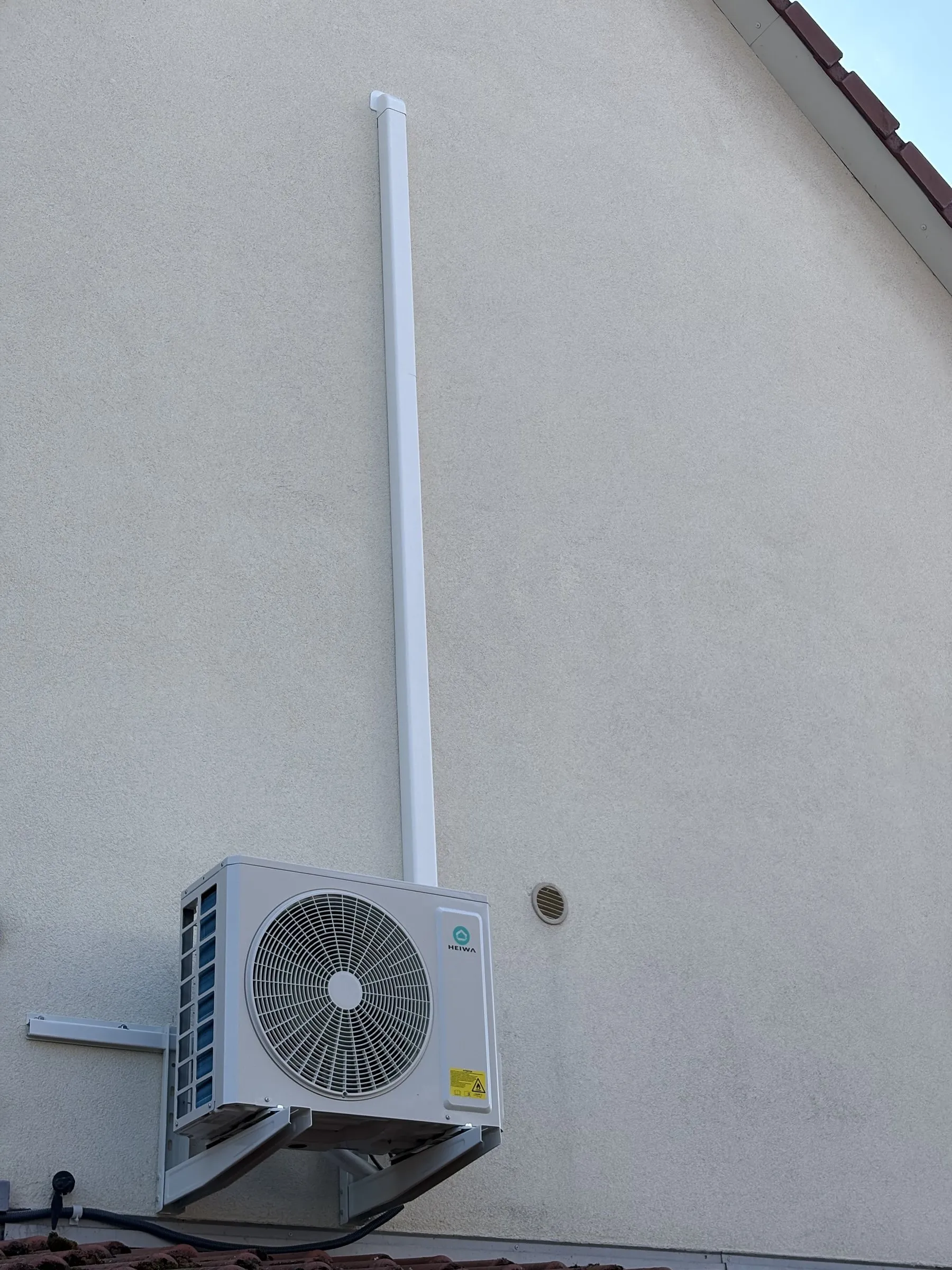 Unité extérieure de climatisation fixée en hauteur sur un pignon enduit
