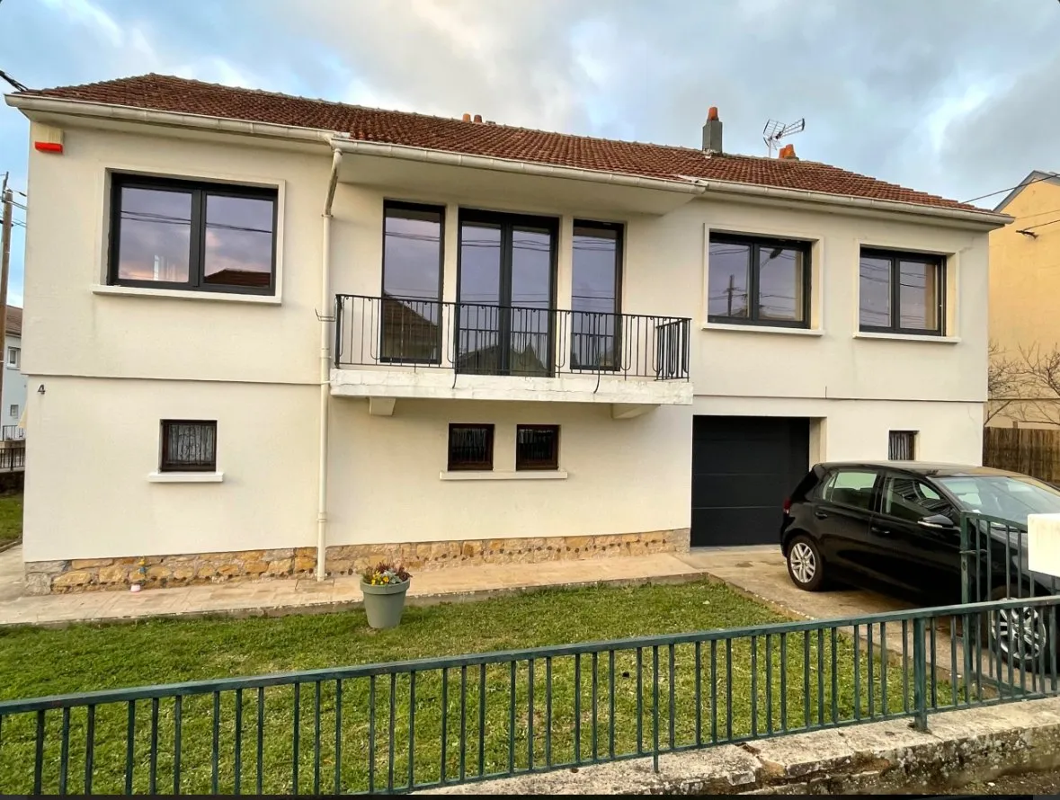 Maison à façade blanche avec balcon, fenêtres noires et porte de garage