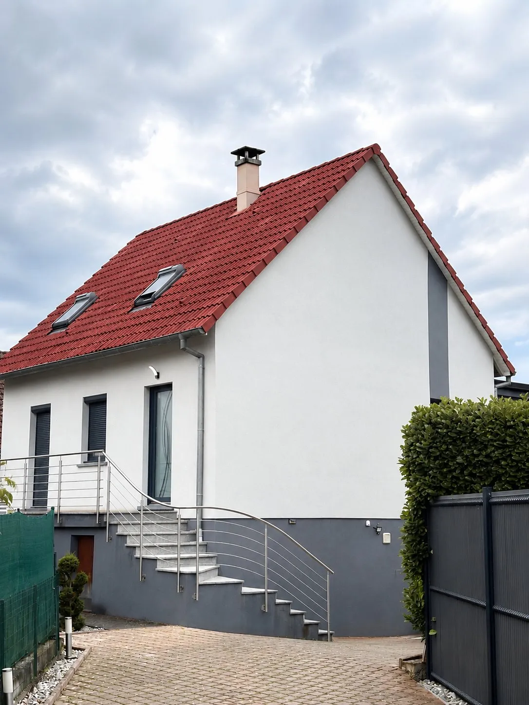 Maison à toit de tuiles rouges, façade blanche et soubassement gris, escalier extérieur