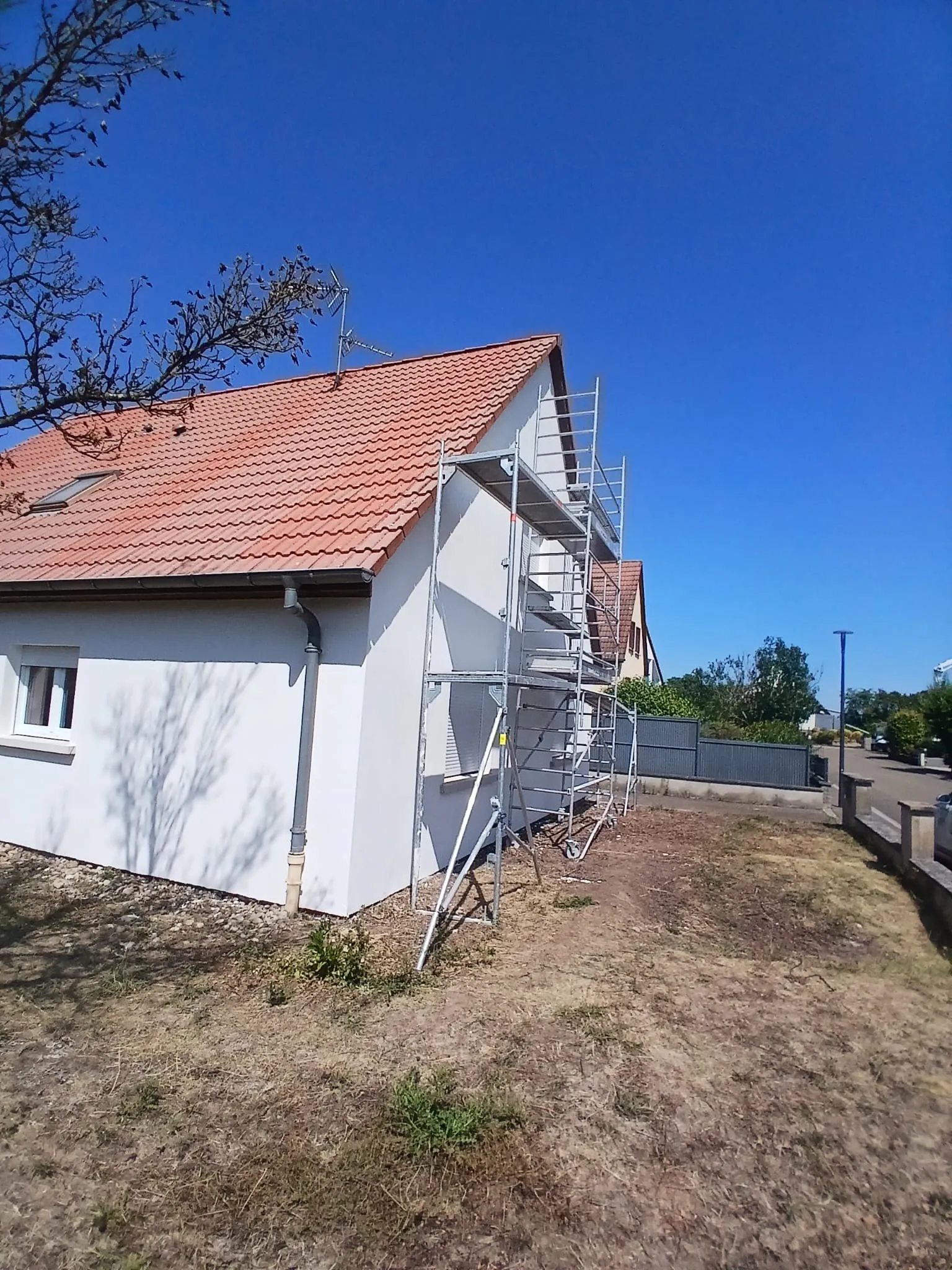 Maison à façade blanche avec échafaudage encore en place sur le pignon