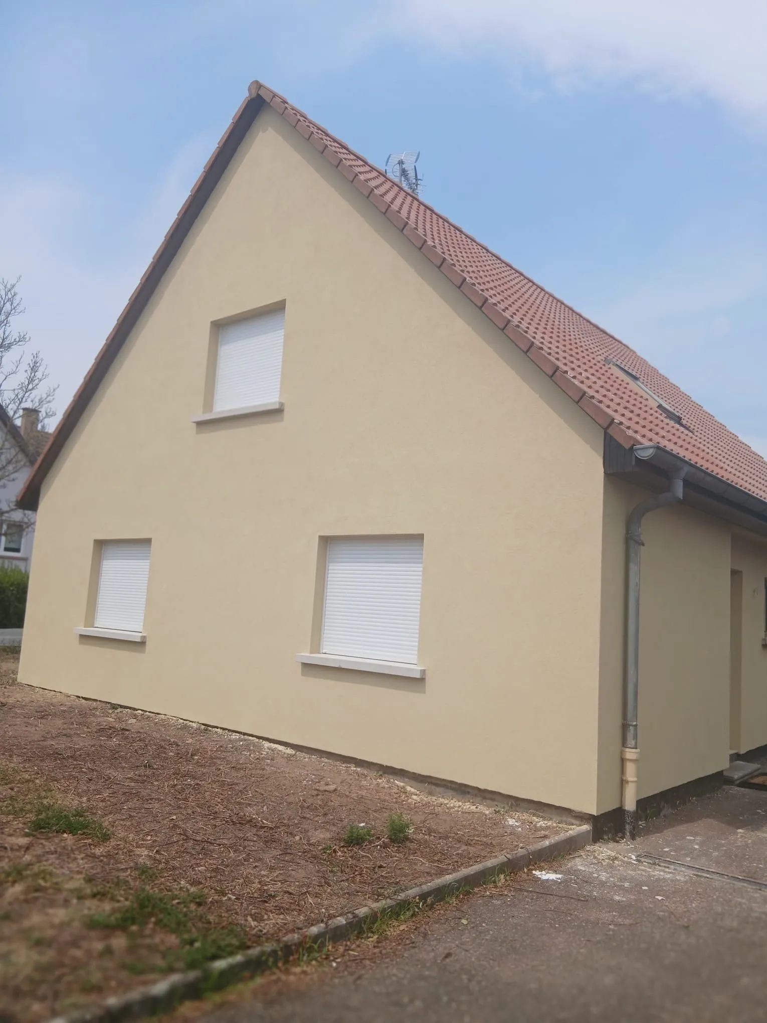 Pignon de maison enduit ton sable, volets roulants blancs