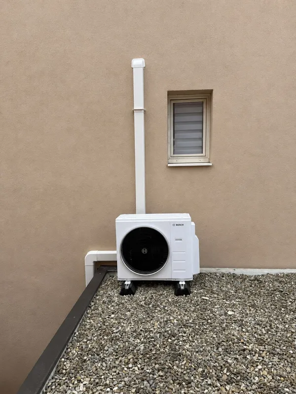 Unité extérieure de pompe à chaleur posée sur gravier contre une façade enduite