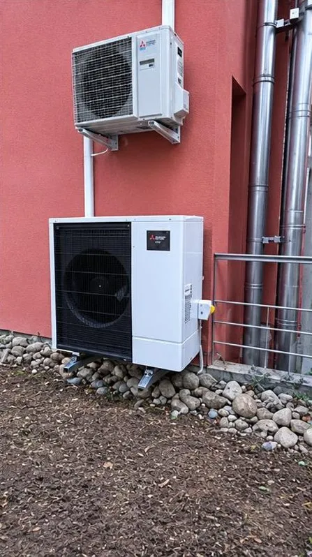Deux unités extérieures Mitsubishi, l’une sur console murale, l’autre au sol, contre une façade rouge