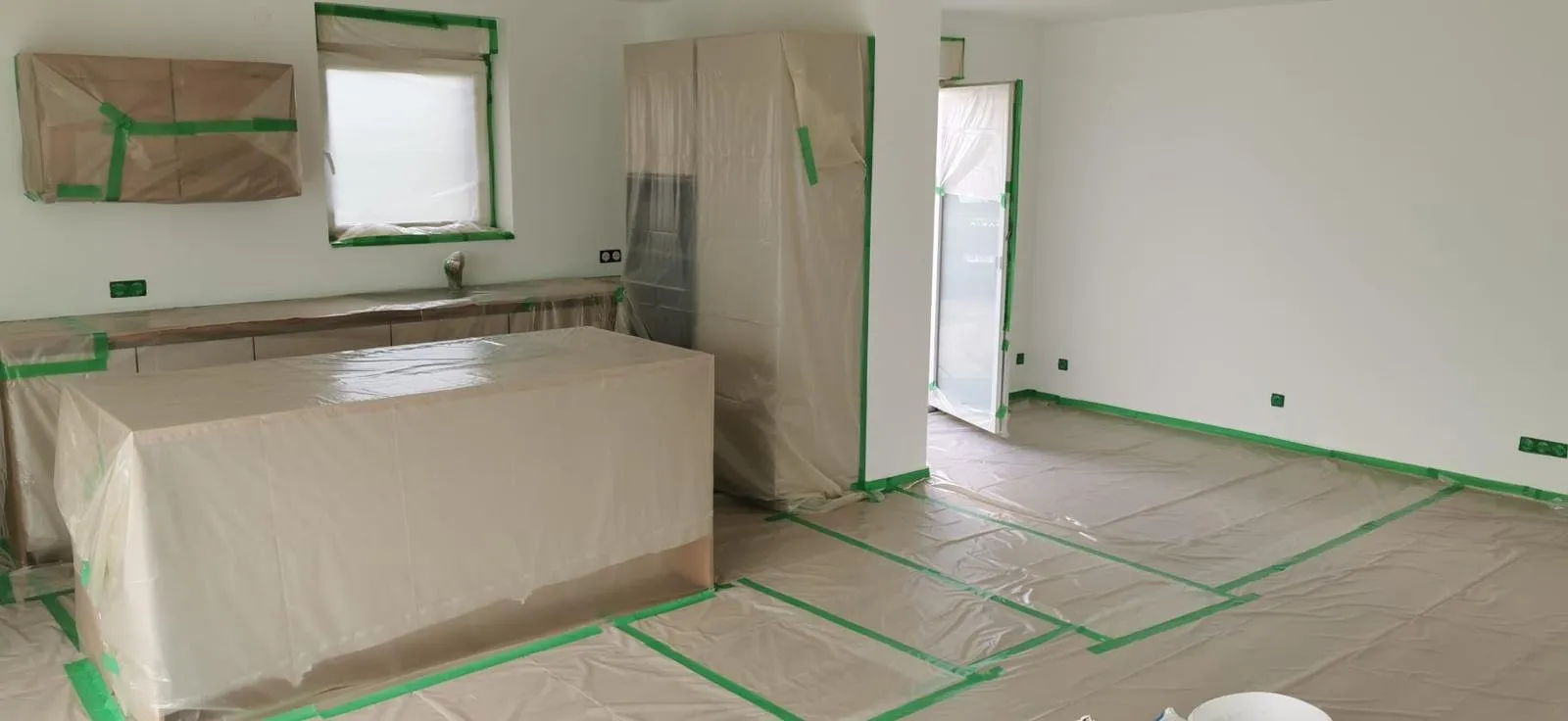 Pièce dont les meubles, la cuisine et le sol sont protégés par des bâches et du ruban avant travaux