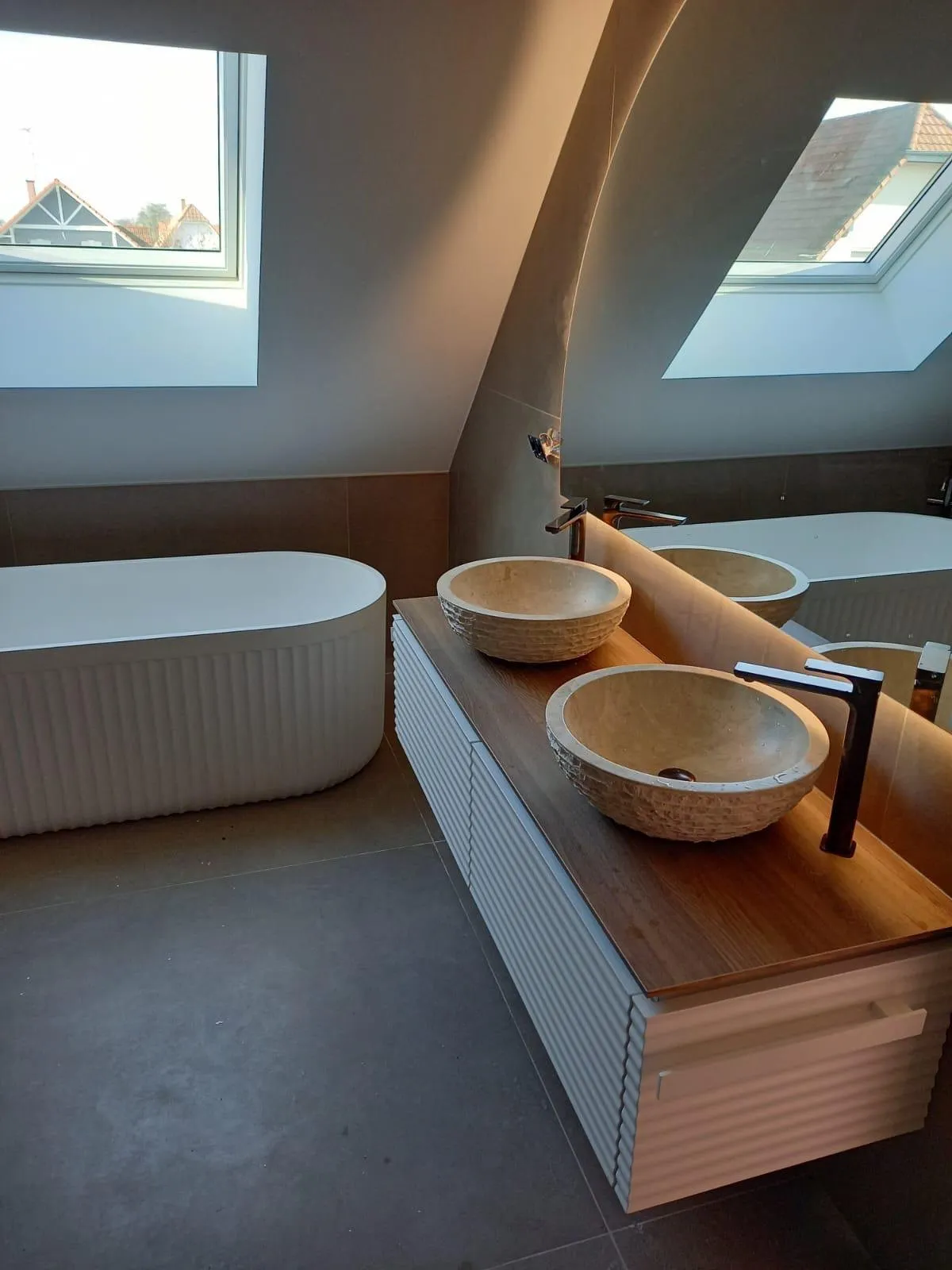 Salle de bains sous combles : baignoire îlot, meuble à double vasque en pierre et fenêtres de toit