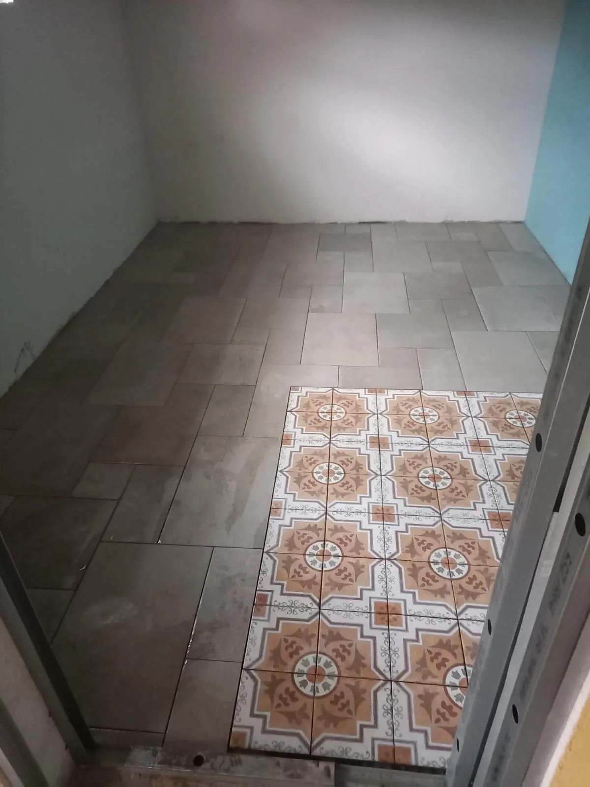 Carrelage de sol gris en cours de pose, avec un tapis de carreaux à motifs